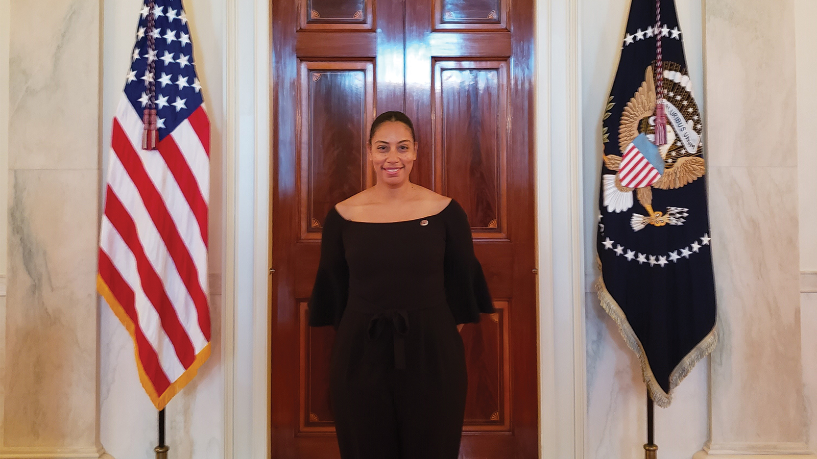 Person pictured standing in front of a door with flags beside it.