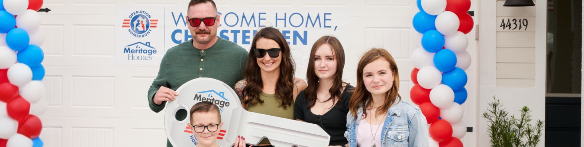 family standing with key in front of home